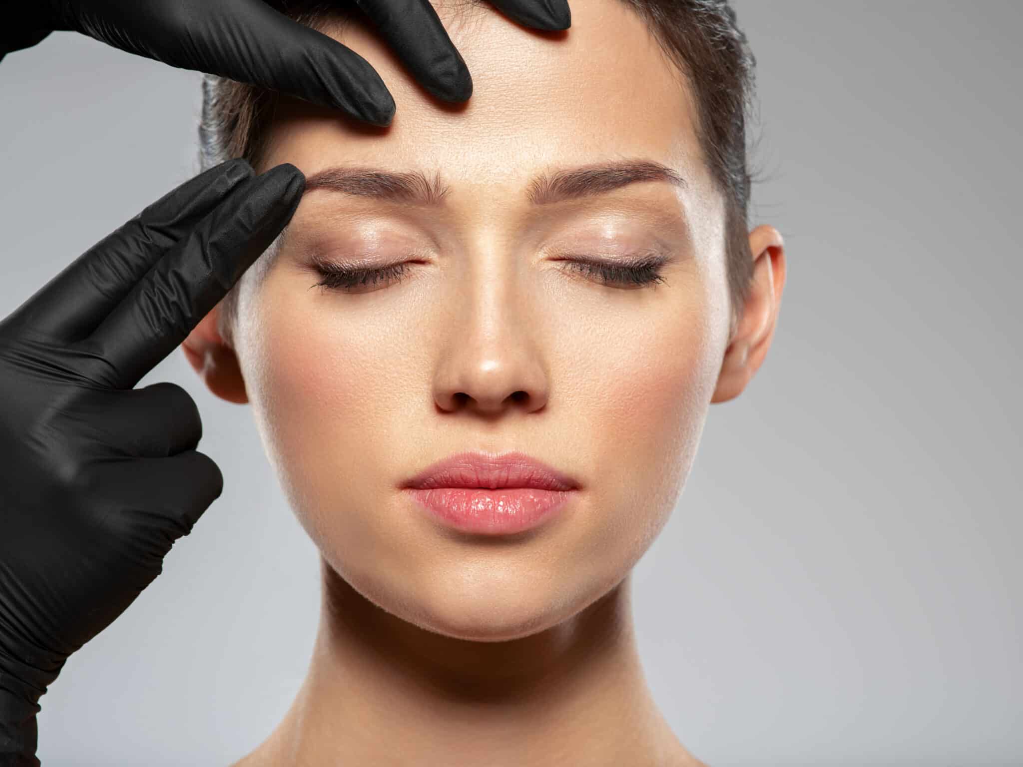 gloved hands looking at a womans eyebrows