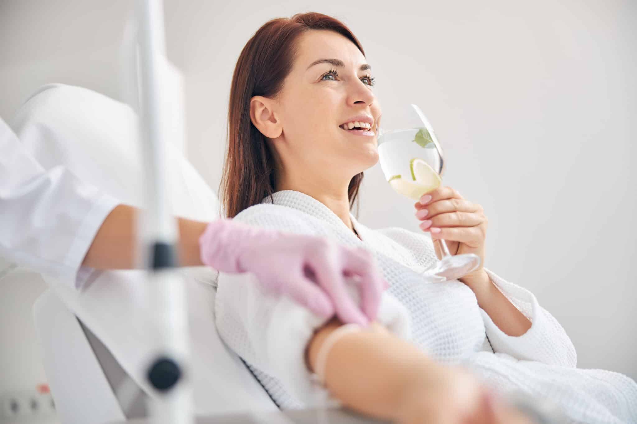 A woman drinking water as she is getting IV hydration Therapy